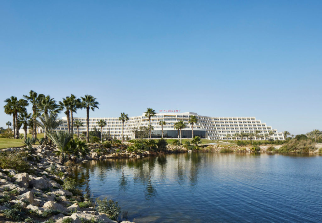 a large white building with palm trees and a body of water