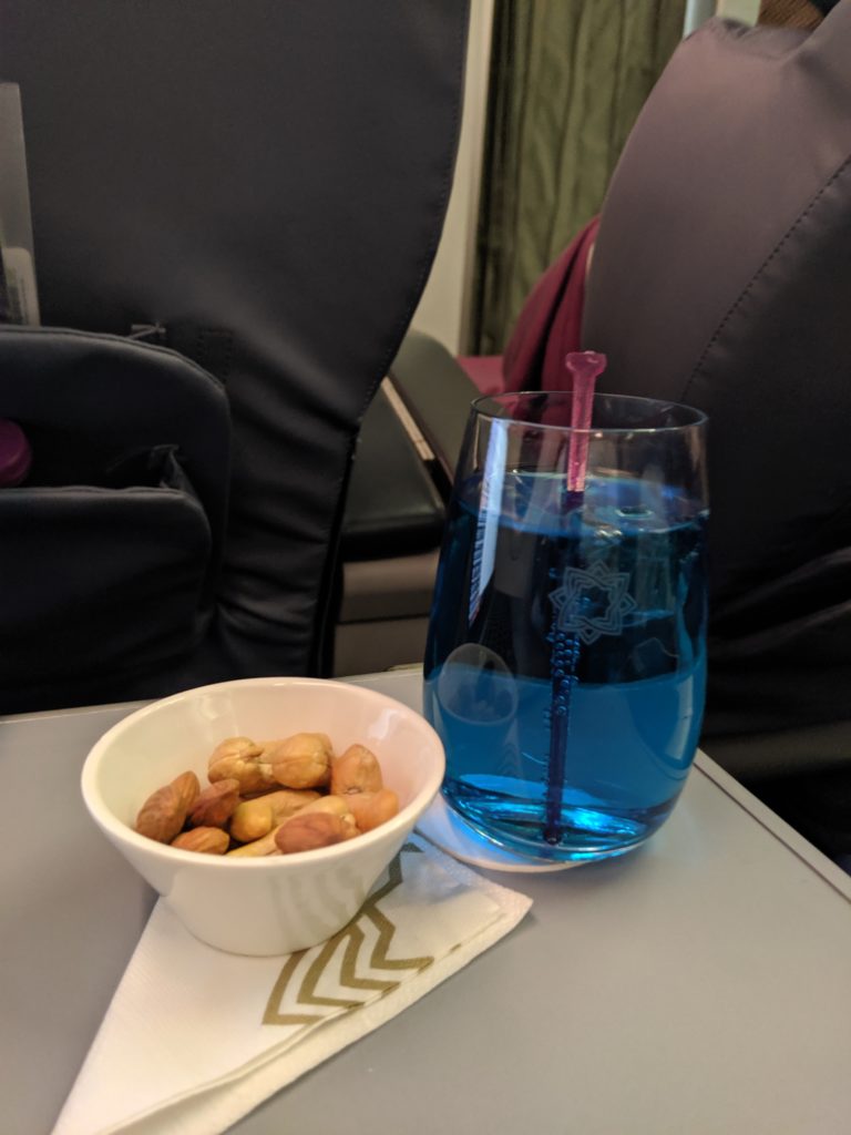 a bowl of nuts and a glass of blue liquid on a table