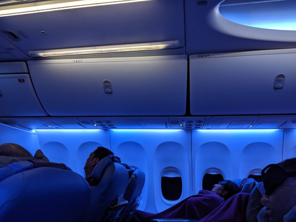 people in an airplane with a blanket sleeping on the seats